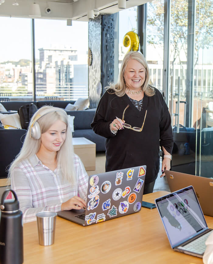 A person standing near a table where people are working on laptops. 