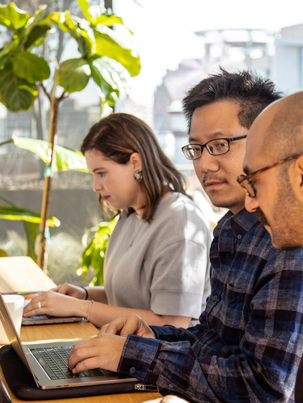 Three people sitting at a conference table staring at laptop screens